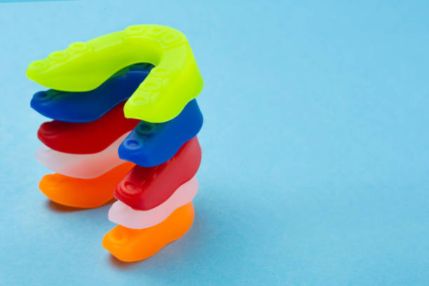 istockphoto-1404043069-612×612 five boxing mouth guards of different colors lie one on top of the other, in a pile, on a blue background, copy space