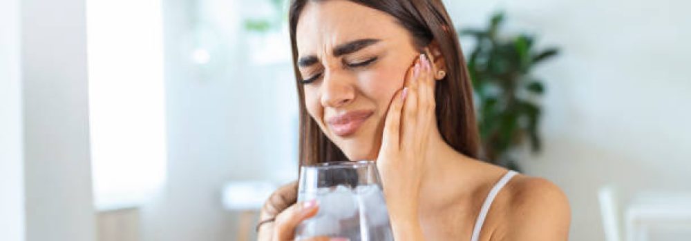 istockphoto-1326020427-612×612 Young woman with sensitive teeth and hand holding glass of cold water with ice. Healthcare concept. woman drinking cold drink, glass full of ice cubes and feels toothache, pain